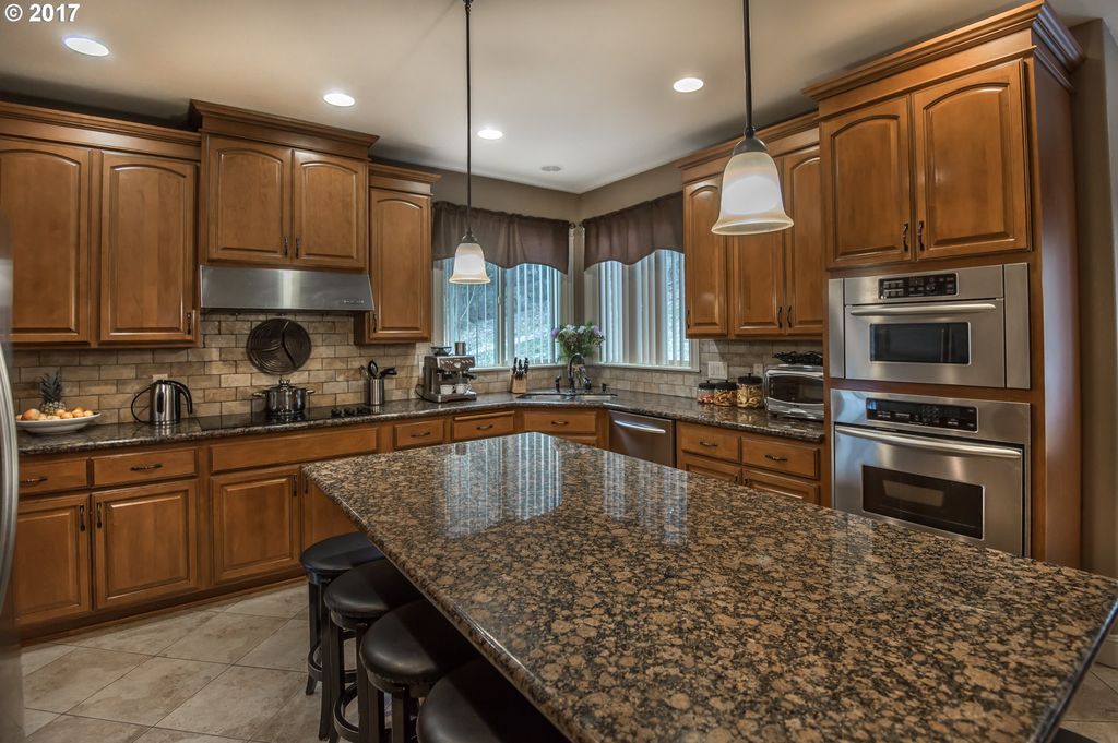Kitchen with speckled brown/black marble, dark wood cabinetry, stainless steel appliances and fixtures in a custom built home