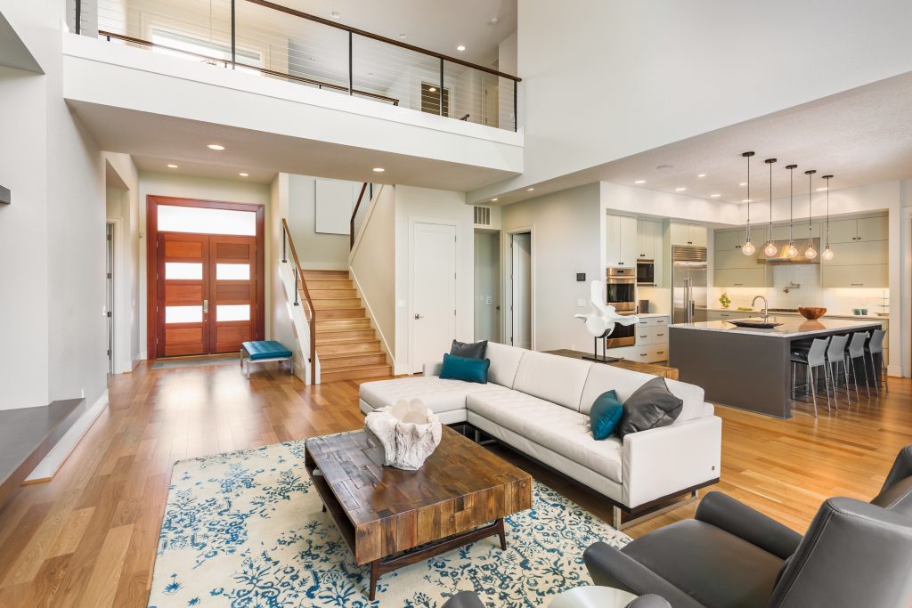 modern living room with oak hardwood flooring, a brown wooden door, stairs and a kitchen in the background