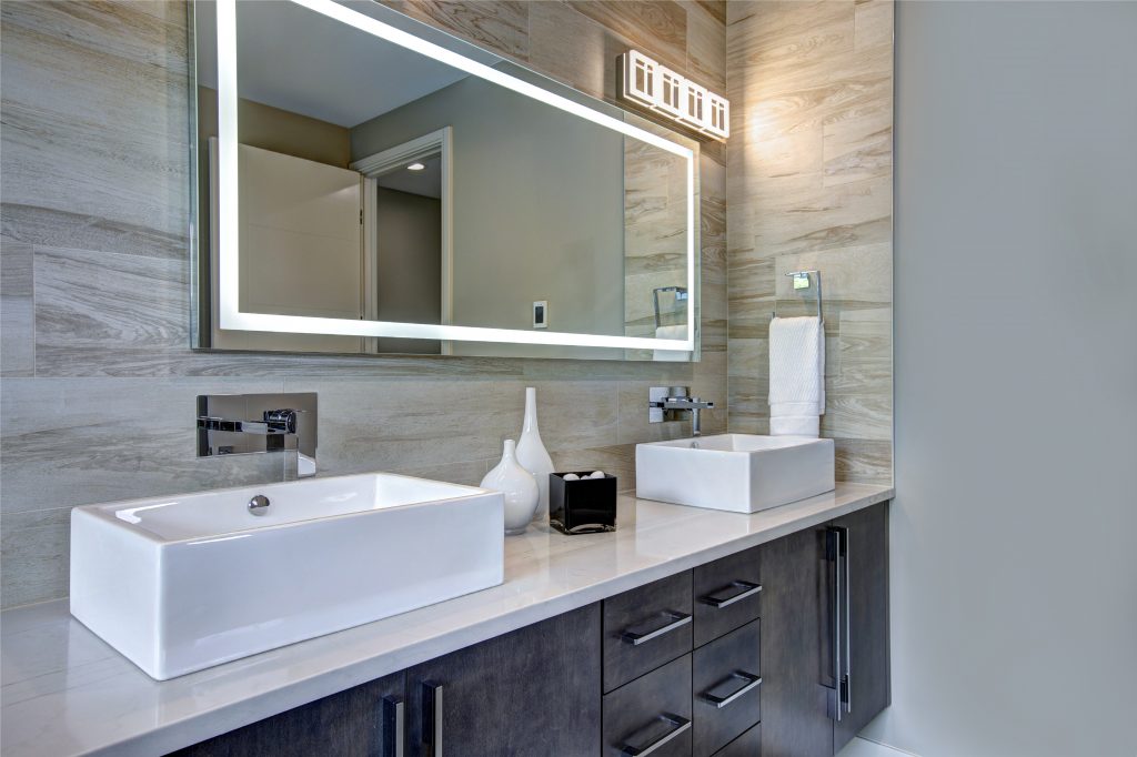 backlit long bathroom mirror with wood on the walls and white sinks